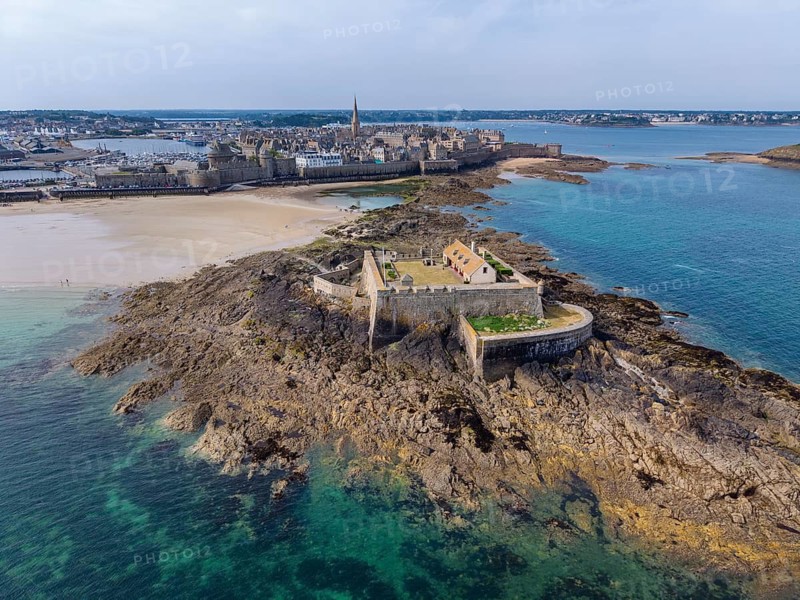 Aerial view of the historic Fort National island fort on the sandy beach of Saint Malo at low tide. Behind it is the distinctive city wall, Les Remparts, which encloses the old town center of the corsair town. Côte d'Émeraude, Emerald Coast, Ille-et-Vilaine Department, Brittany, English Channel, France