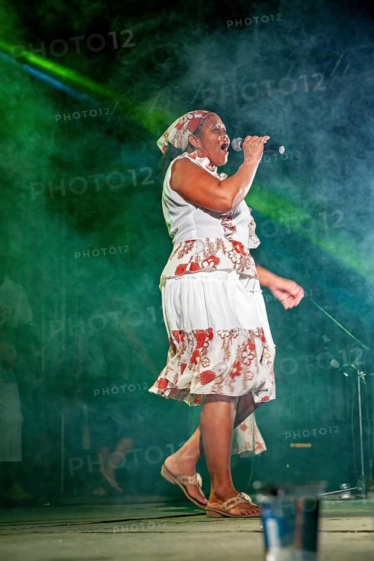 Woman in a floral print dress sings passionately on an illuminated stage, a band plays and dances at a festival in Petrolina in Brazil