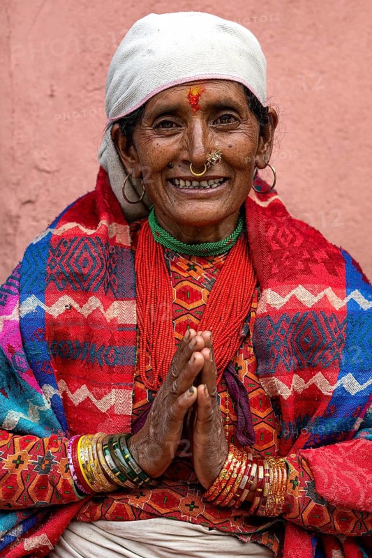 Portrait of friendly smiling elderly woman with traditional jewelry folding her hands in greeting Namaste, Hindu ethnic group, Himalayas, Simikot, Humla region, western Nepal, Nepal