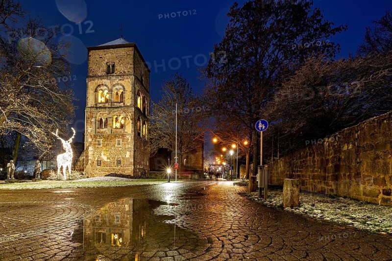 A stone tower illuminated at dusk, surrounded by cobblestones and sculptures, The tower of the Abbey Ruins of Bad Hersfeld