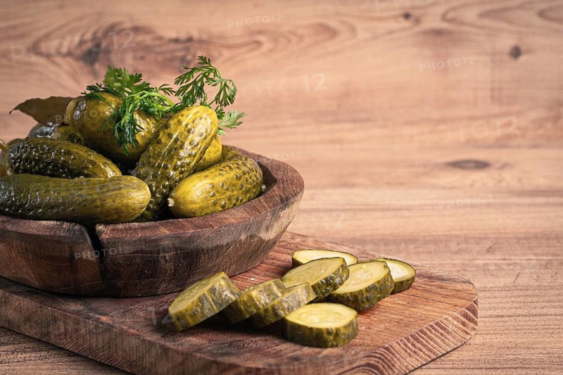 Pickled cucumbers in a wooden bowl with herbs and spices, close-up, rustic style
