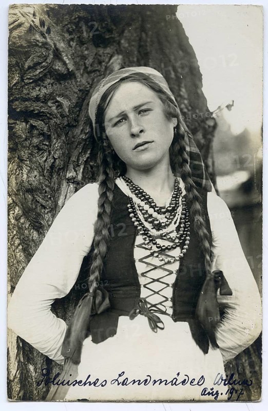 Poland, country girl, Vilnius, Lithuania, World War I, young girl in traditional dress with long braids standing in front of a tree, 1917