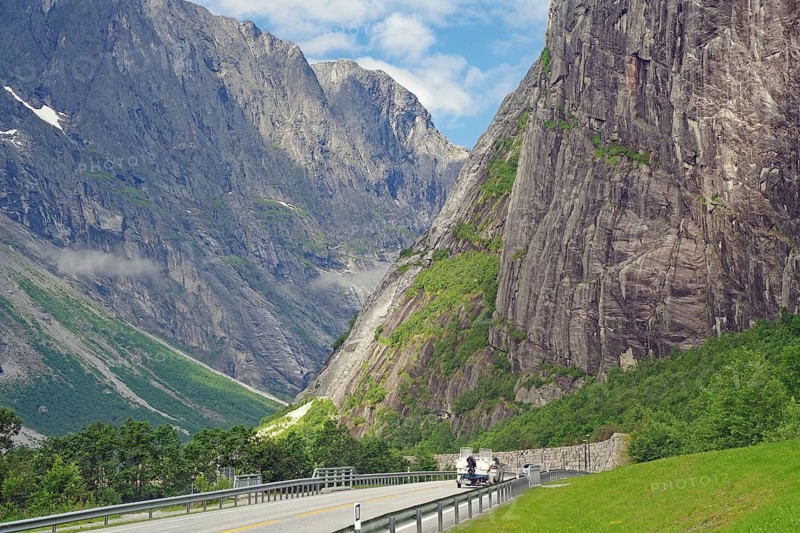 Motorcyclists on a lonely mountain road, flanked by steep cliffs and green mountains under a blue sky, Tom Cruise filming location, Raumadalen, Trollvegen, Andalsnes, Norway