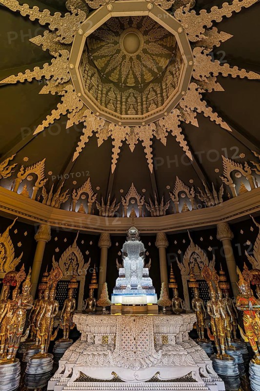 Glass Buddha statue surrounded by figures as heavenly beings and temple guards in the public prayer hall in the Buddhist temple complex Wat Phra That Don Phra Chan, near Lampang, Lampang Province, Thailand