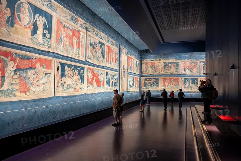 Museum visitors, tourists look at the illuminated, colorful image segments of the historic 14th-century Apocalypse tapestry on a long wall area, Château d'Angers, Angers Castle, Angers, Maine-et-Loire department, Pays de la Loire region, France