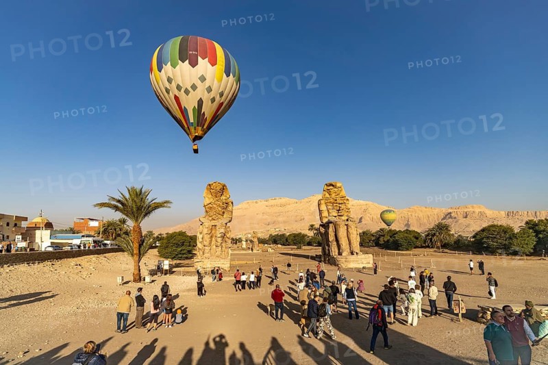 Travel groups and hot air balloon at the Colossi of Memnon in the Nile Valley in West Thebes near Luxor, Egypt