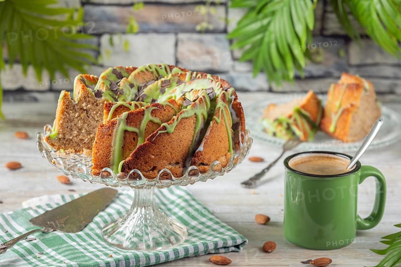 A sliced cake with green icing next to a cup of coffee and almonds