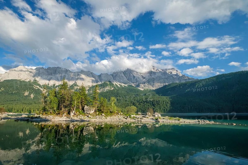Symmetrical mountain reflection in the calm waters of Eibsee lake framed by green trees in the Bavarian Alps, Germany