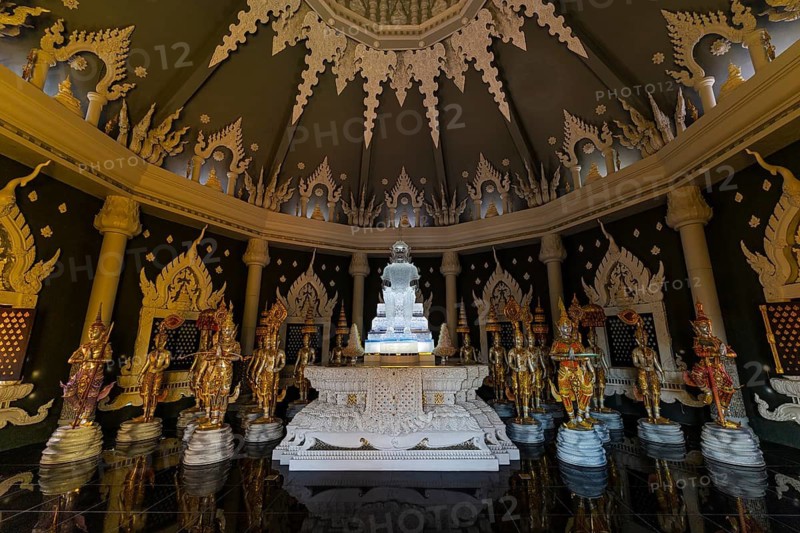 Glass Buddha statue surrounded by figures as heavenly beings and temple guards in the public prayer hall in the Buddhist temple complex Wat Phra That Don Phra Chan, near Lampang, Lampang Province, Thailand