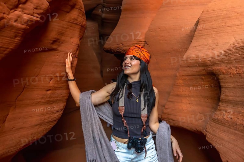 Woman exploring antelope canyon's sculpted orange and red sandstone walls, touching formations and smiling while soaking in the desert light, shadow and geological beauty