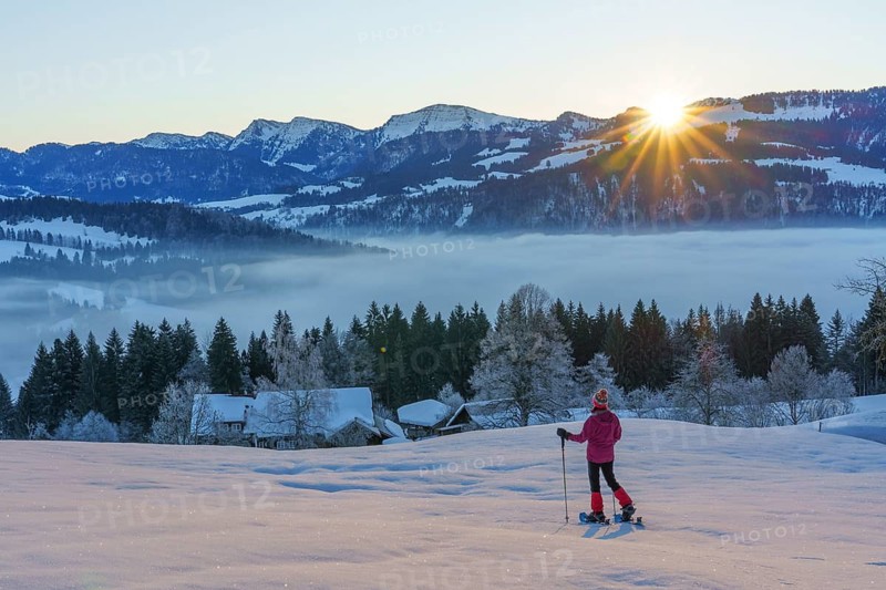 Landscape with woman watching sunrise over the Nagelfluh mountain chain during a snowshoe hike in the Allgaeu Alps near Oberstaufen, Bavaria, Germany