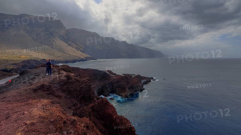 Punta de Teno, person standing on rocky coast with views of dramatic mountains and clouds over the sea, Masca, Barranco de Masca, canyon, Teno, Teno Mountains, northwestern Tenerife, Tenerife, Canary Islands, Spain