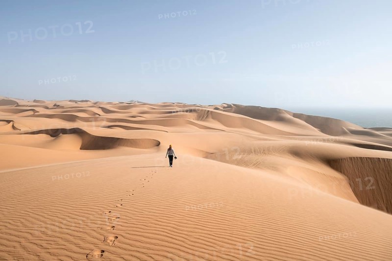 Woman with camera, lonely person walking across dunes, sand dunes with wave pattern, dune sea, sandy desert, impressive desert landscape, Namib Naukluft Park, Namib Desert, Namibia