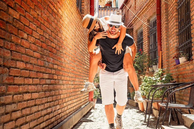 Portrait of carefree Playful caucasian couple enjoying piggyback ride together time in old town Tbilisi Mtatsminda local hidden gem area. Friends having fun bonding explore travel together in caucasus