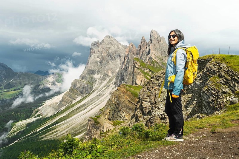 Happy female traveler yellow backpack stand on famous viewpoint ridge line Seceda South Tyrol Dolomites Italy looking up feeling free peaceful active lifestyle outdoor vacation