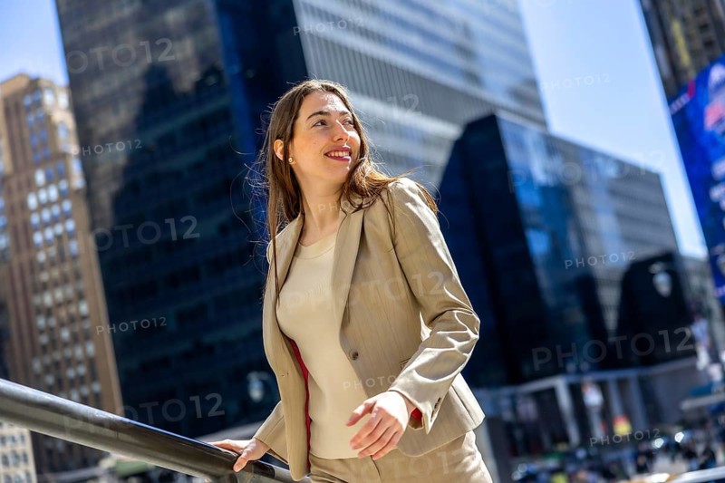 Professional woman enjoying the urban atmosphere, leaning on a railing with skyscrapers reflecting the bright sky, radiating confidence and success in the bustling city