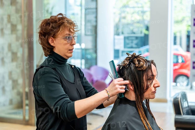 Professional hairdresser carefully styling and trimming a young woman's wet hair with scissors and a comb, providing a fresh haircut service in a modern beauty salon environment