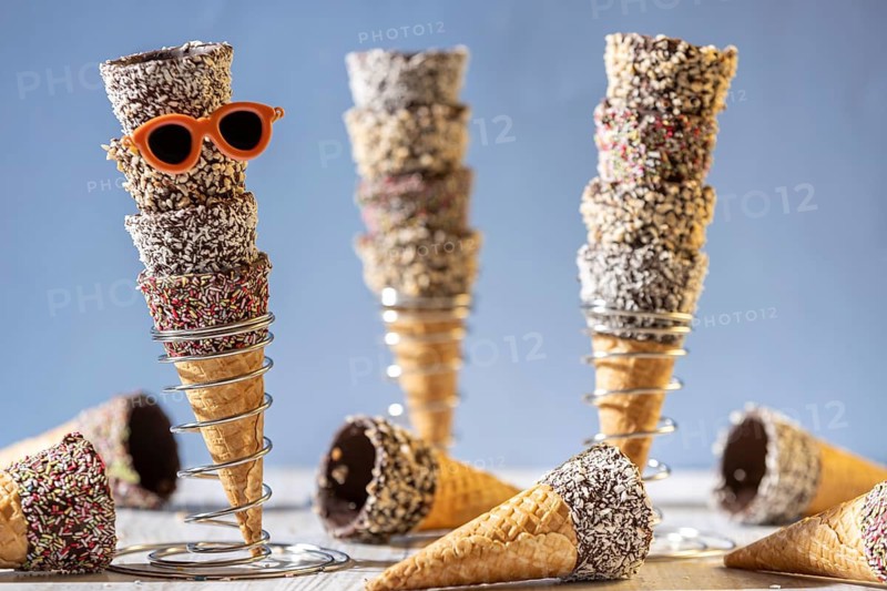 Ice cream cones stacked in metal stands, decorated with sprinkles, nuts and sunglasses