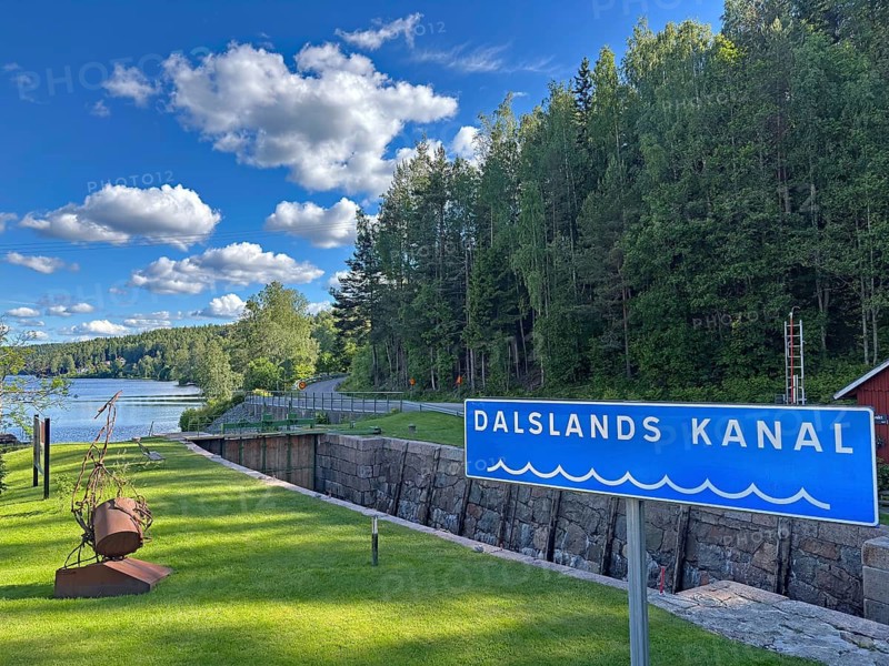 Dalslands canal sign against wooded background and river. Clear sky with few clouds, Dals-Rostock, Dalsland Canal, Dalsland, Mellerud Municipality, Sweden