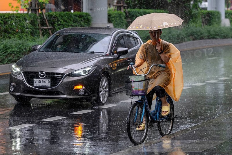 Female cyclist and passenger car in rain, Bangkok, Thailand