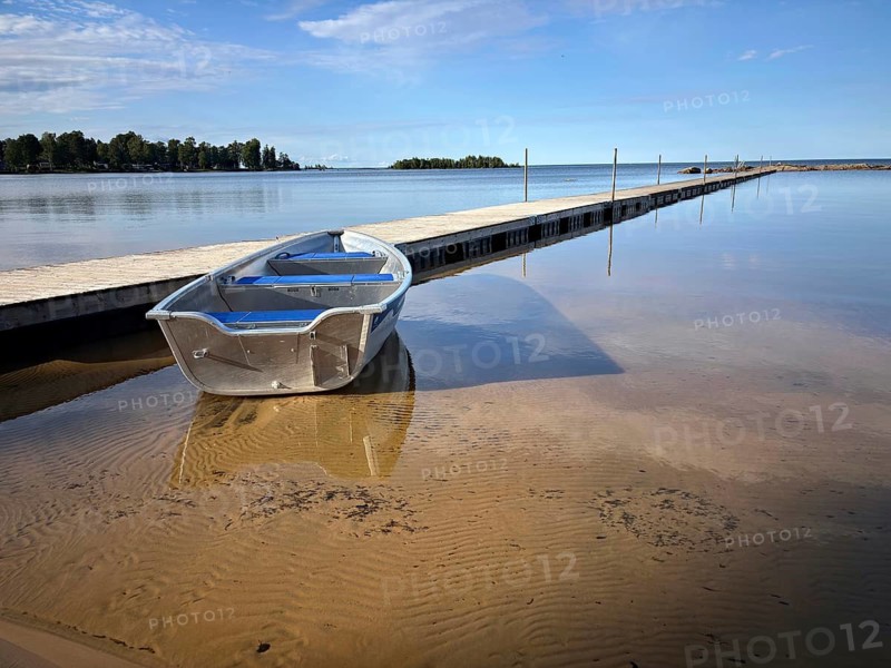Lonely boat on a sandy beach next to a jetty. Blue sky and calm water surface, Vänern, Mellerud, Dalsland, Sweden