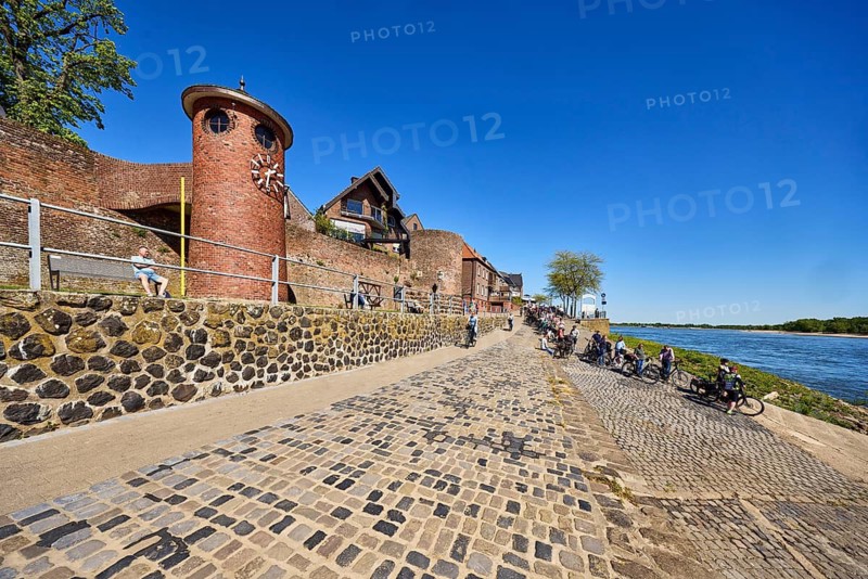 Rhine river, Rees Rhine level, level tower, water meter, ferry dock, general architecture, houses, quarry stone wall, waterfront, footpath and cycle path, cyclists, trees, blue sky, cloudless, Rhine promenade, Rees, Kleve district, North Rhine-Westphalia, Germany
