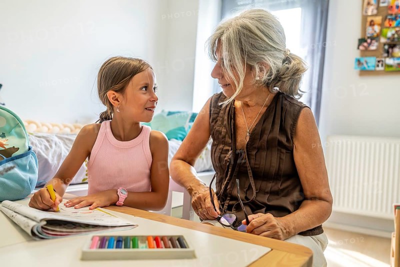 Grandmother and granddaughter bonding, sharing creative moments while drawing at a table, representing family love, education, and intergenerational connection in a domestic setting