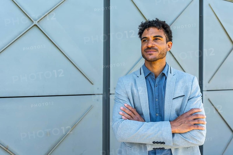 Professional young man with curly hair and a subtle smile, standing confidently with arms crossed, looking away, reflecting leadership and future vision