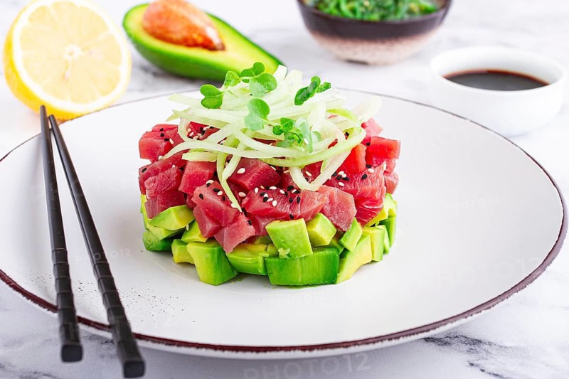 Fresh tuna tartare with avocado served on a marble table with soy sauce and seaweed salad