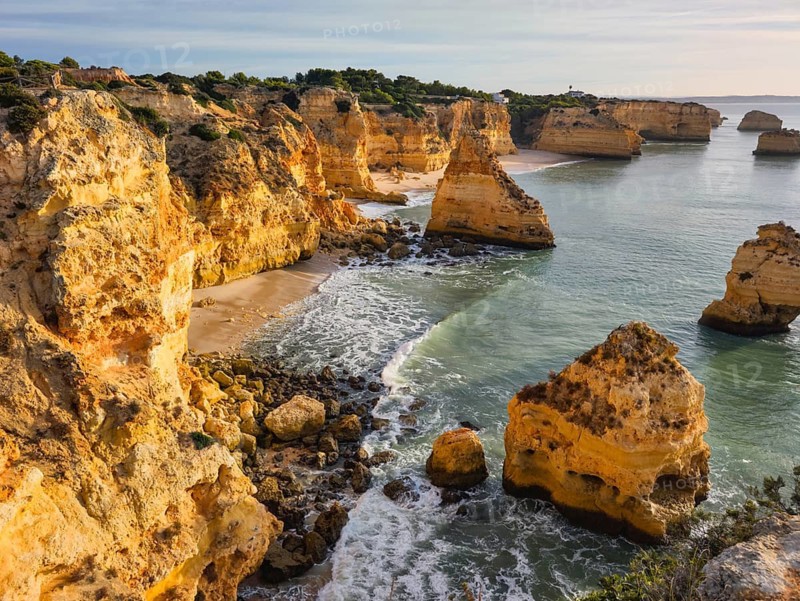 Sunrise view of Praia da Marinha beach in Algarve, Portugal, with golden cliffs, sea stacks, Atlantic waves, turquoise water, and a rocky cove