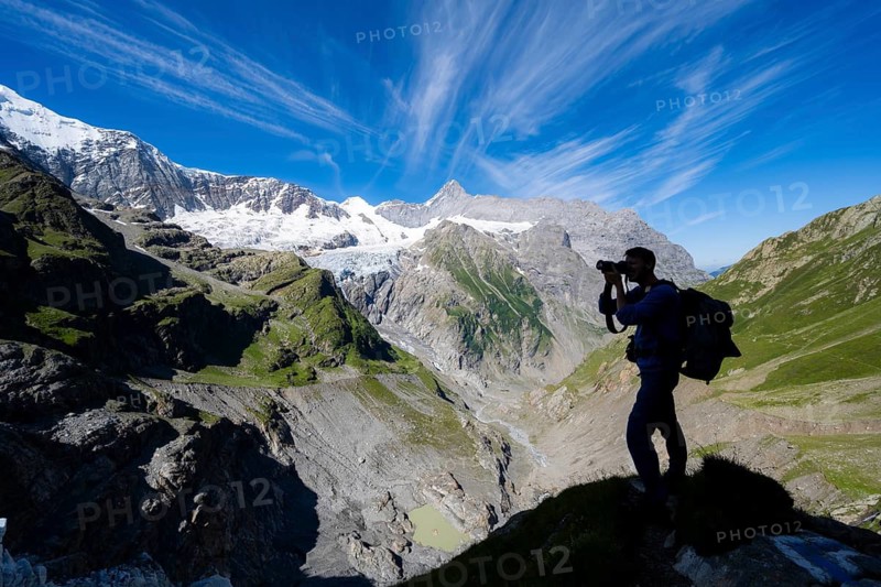 Silhouette of photographer with camera in front of mountain panorama, picturesque high alpine mountain landscape with Grindelwald-Fiescherfirn glacier, hiking to Schreckhornhütte, Bernese Oberland, Switzerland