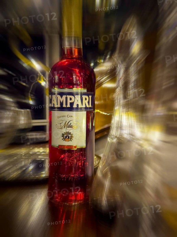 Campari bottle with carafe on wooden counter, evening mood, zoom effect