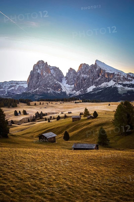 Light from sunrise on the mountains and quiet meadow landscape, view over the autumnal Seiser Alm on Sassolungo and Plattkofel, alpine huts, Dolomites, South Tyrol, Italy