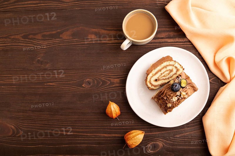 Sweet loaf with cream and caramel, cup of coffee, on brown wooden background with orange textile, copy space, top view, flat lay