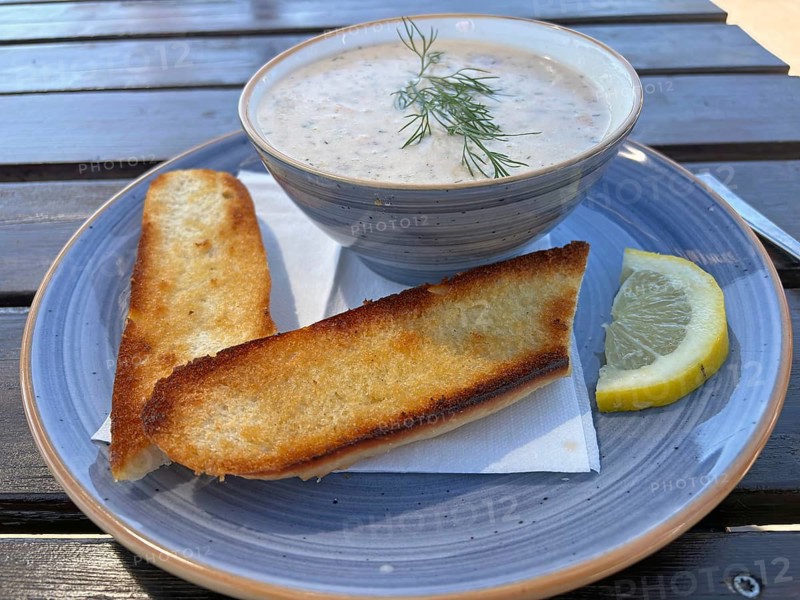 Creamy soup with dill and toasted bread on a plate next to a slice of lemon on a wooden table, Ölandsleden, Öland, Sweden