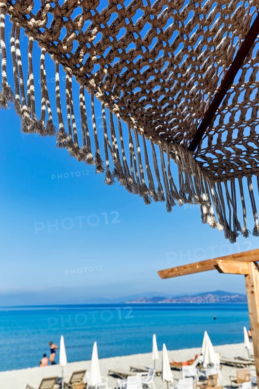 Macrame parasol with fringes, boho chic style, natural design, decoration, picturesque view from a beach club of the sandy beach and the blue Mediterranean Sea, L'Île-Rousse, Haute-Corsica, Corsica, France