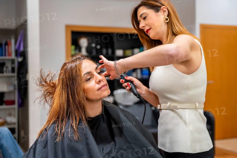 Hairdresser working on a client's wet hair, holding a curling iron and preparing to style, providing a beauty treatment in a modern hair salon environment