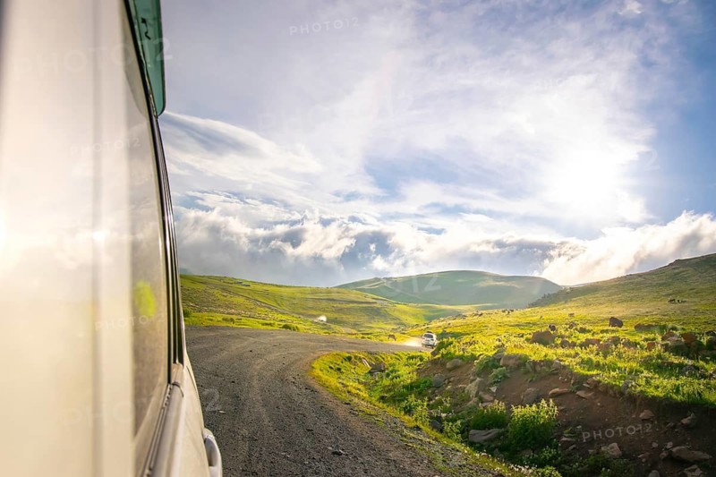 White car drives on caucasian green wilderness with sky and meadow view. Tusheti. Georgia