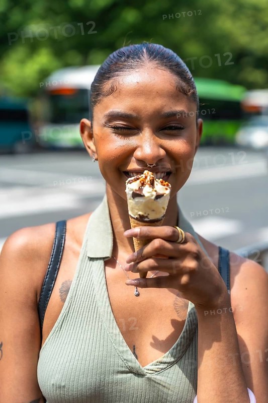 Young woman smiling while holding and eating an ice cream cone outdoors on a city street, conveying concepts of summer fun, urban lifestyle, happiness, and refreshment