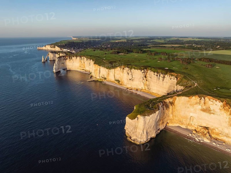 Aerial view of the distinctive Pointe de la Courtine ledge in the evening sun, then the La Manneporte rock gate behind it the Porte d'Aval rock formation, well-known sights on the chalk coast with the distinctive rock pin, behind it the holiday resort of Étretat with the beach, on the horizon the Falaise d'Amont cliffs, right on the cliffs of the Golf d'Étretat golf course founded in 1908, Alabaster Coast, La Côte d'Albâtre, chalk cliffs, English Channel, Seine-Maritime, Normandy, France