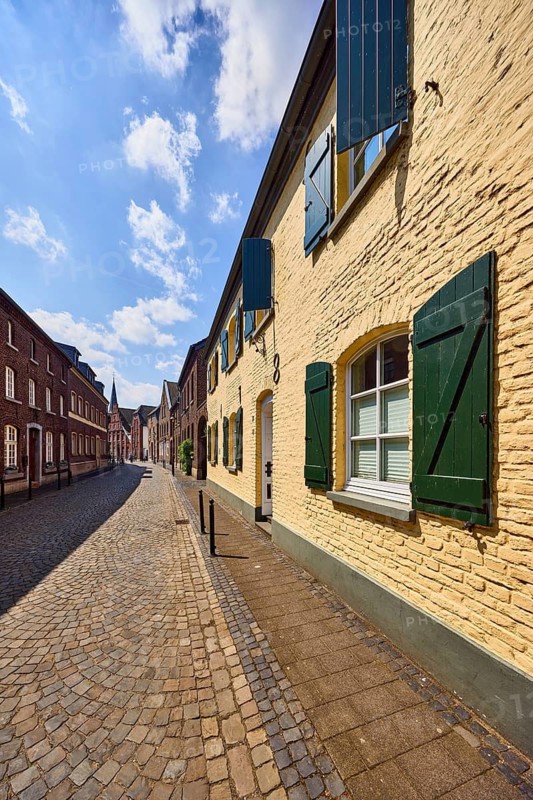Street, historic brick buildings, buildings, houses, façade with windows and shutters, barrier bollard, sidewalk, street, paving stones, blue sky, cumulus clouds, Feldstraße, Wachtendonk, Kleve district, North Rhine-Westphalia, Germany