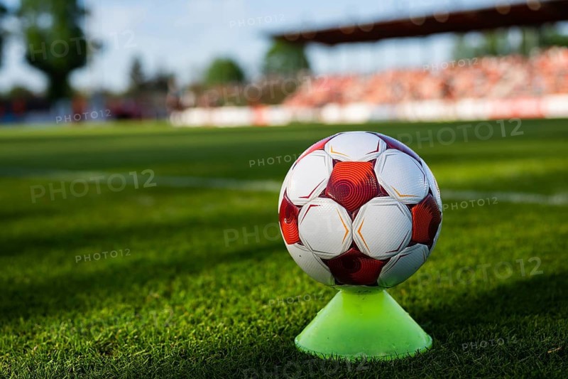 Red and white soccer ball placed on a training cone on a grass pitch with stadium seating in the background in Glogow, Poland