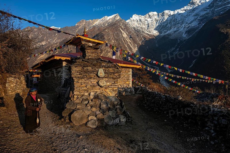 Young woman next to a small Buddhist monastery with manistones in the evening light, Nepalese, local of the Tsumba Tibetan ethnic group traditionally spinning wool with a spindle, Tsum Valley, Himalayas, Nepal