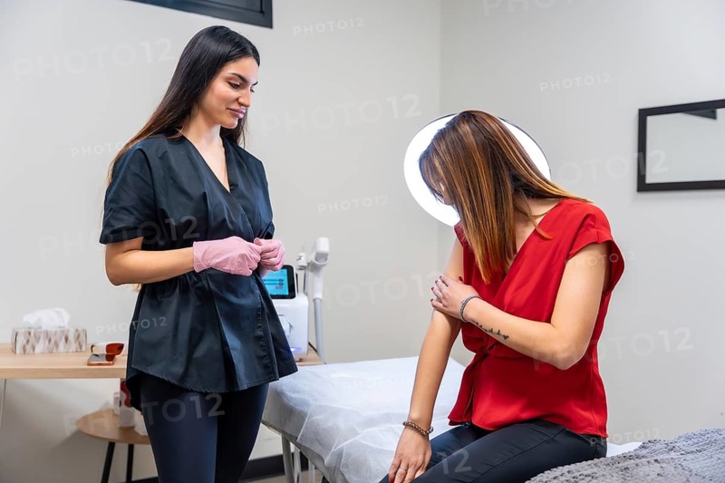 Medical specialist in a clinic explaining a tattoo removal procedure or aesthetic treatment to a female patient, focusing on the consultation and discussion before a cosmetic session