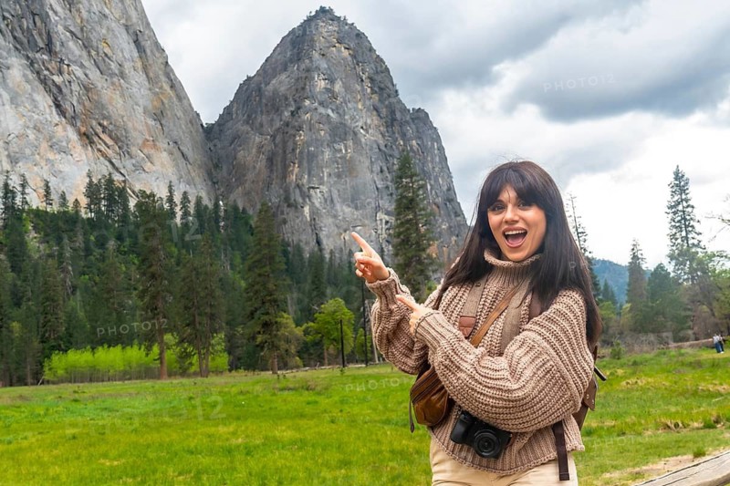 Young woman traveler pointing with both hands, expressing excitement and discovering the iconic granite cliffs, green forest, and vast natural beauty of yosemite national park