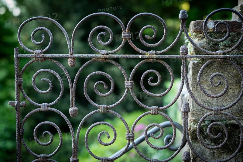Close-up view of a rusty iron gate with spirals against a blurred green background, Bardini Garden or Giardino Bardini, Florence