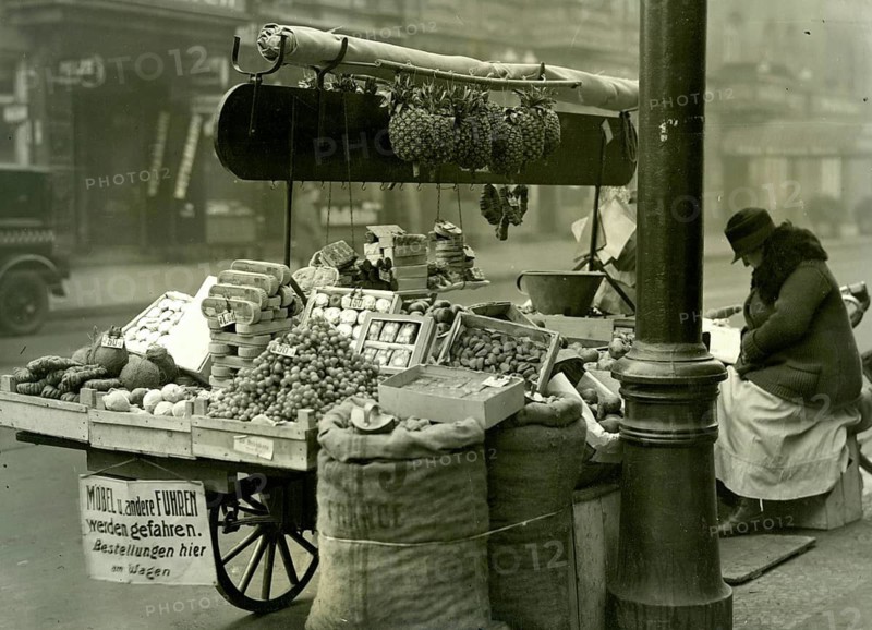 Berlin, fruit truck, job, poverty, street sales, pineapple, woman, fruit and vegetable stand with a saleswoman sitting on a busy street, twenties, Sasha Stone, around 1928
