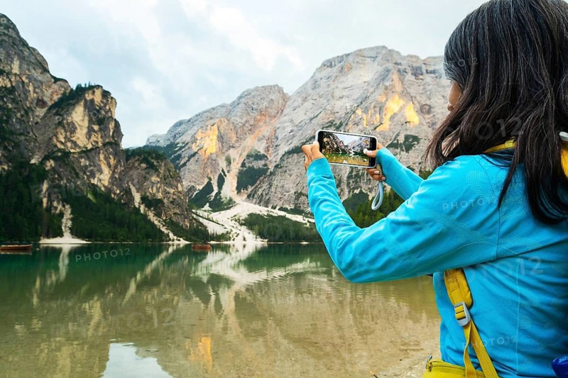 Close up Woman hiker enjoy taking smartphone photo of Lago di Braies alpine lake turquoise water mountain reflections Dolomites Italy