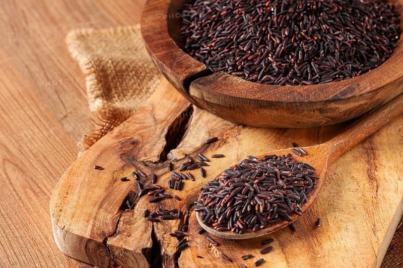 Natural black rice in a wooden bowl and spoon on a wooden surface in rustic style, top view