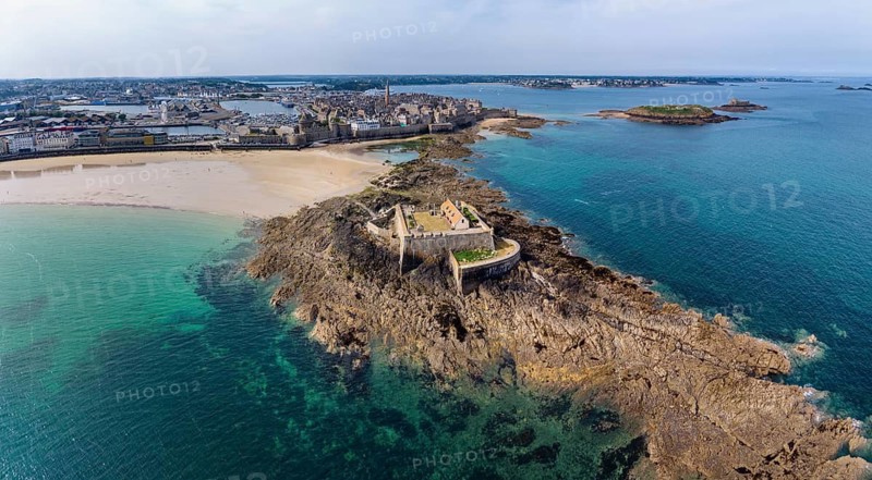 Aerial view, panorama of the historic Fort National island fort on the sandy beach of Saint Malo at low tide. Behind it is the distinctive city wall, Les Remparts, which encloses the old town center of the corsair town. Côte d'Émeraude, Emerald Coast, Ille-et-Vilaine Department, Brittany, English Channel, France